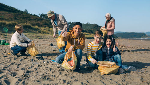 Portrait of cheerful siblings picking garbage at beach