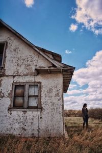 Full length of woman standing on field beside an abandoned house 