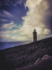 Lighthouse amidst sea and buildings against sky