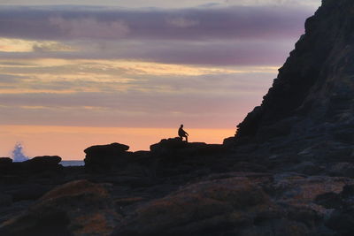 Silhouette rocks on cliff against sky during sunset
