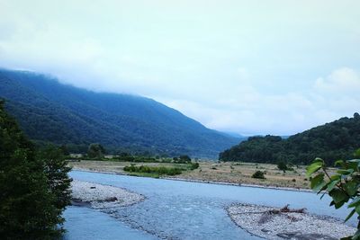 Scenic view of river by mountains against sky