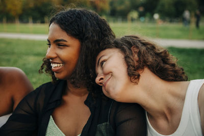 Smiling teenage girl leaning on friend's shoulder at park