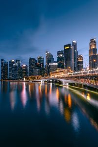 Illuminated buildings by river against sky in city at night