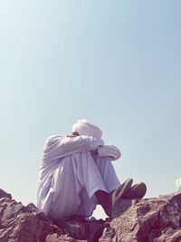 Rear view of woman sitting on rock against clear sky