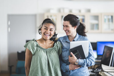 Portrait of smiling teenage student standing with teacher in computer lab at high school