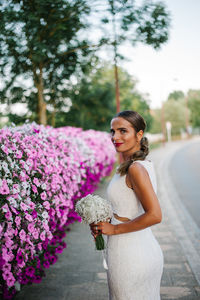 Portrait of bride standing by pink flowers against sky