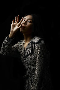 Portrait of young woman looking away against black background