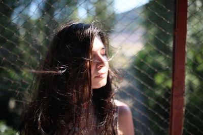 Beautiful woman with eyes closed against chainlink fence