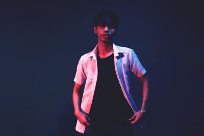 Portrait of young man standing against black background