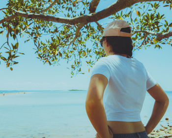 Rear view of woman standing by sea against sky