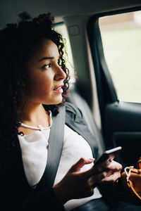 Mid adult businesswoman looking away sitting with smart phone in taxi