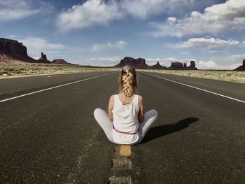 Rear view of woman sitting on road against sky