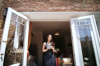 Smiling woman standing on doorway during sunny day