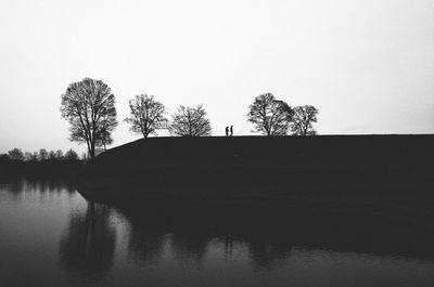 Low angle view of silhouette trees by lake against clear sky