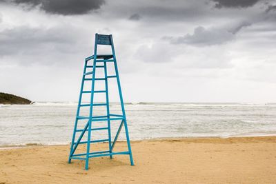 Empty blue lifeguard chair at beach against sky