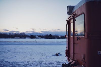 Train on snow covered landscape against sky during sunset