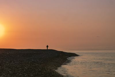 Silhouette man standing on shore against sky during sunset