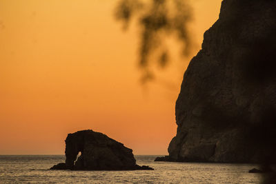 Silhouette rock formation by sea against sky during sunset