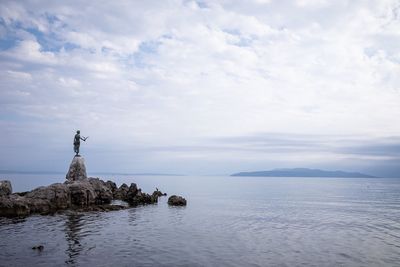 Statue on rock by sea against sky