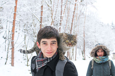 Portrait of smiling young woman standing by tree during winter