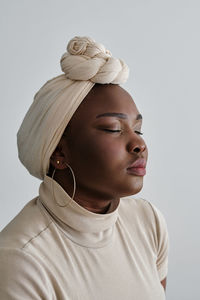 Gorgeous young african female model in stylish traditional turban standing against white background with closed eyes