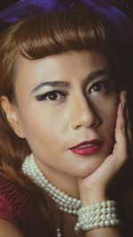 Close-up portrait of woman wearing jewelry and make-up against black background