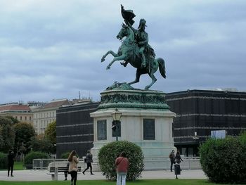 Statue in front of building against cloudy sky