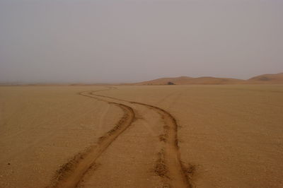 Tire tracks at sandy desert against sky