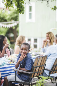 Smiling boy eating watermelon while sitting with family in garden party