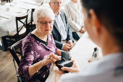 High angle view of owner holding credit card reader while senior woman paying in restaurant