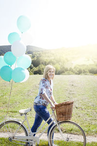 Full length portrait of smiling young woman with bicycle on grassy field