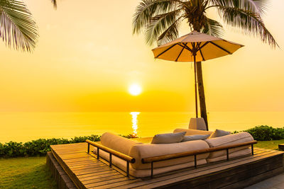 Lounge chairs by swimming pool against sky during sunset