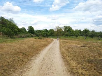 Dirt road amidst trees on field against sky