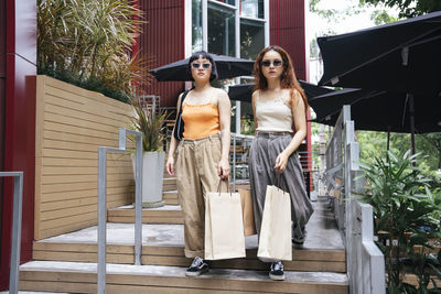 Portrait of lesbian couple holding shopping bags walking on steps outdoors