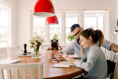 Man assisting daughter while girl using digital tablet in background at home