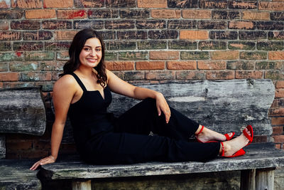 Portrait of young woman sitting against brick wall