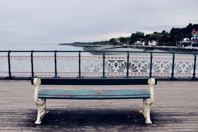 Empty bench by sea against sky