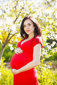 Portrait of smiling woman standing by red flowering plant