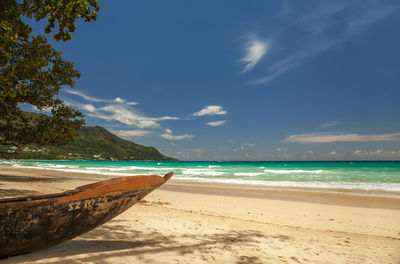 Wooden vessel at tree framed white beach at sunny day with clear sky and some white clouds