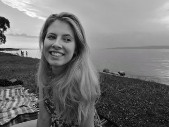 Smiling young woman looking away by sea against sky