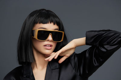 Portrait of young woman wearing sunglasses against black background