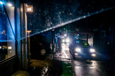 Illuminated car headlight on street during rainfall at night