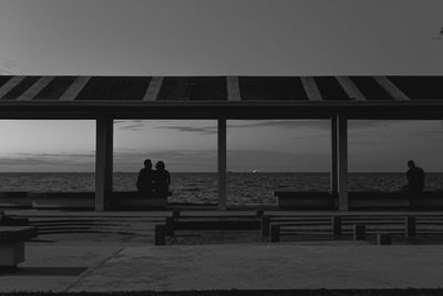 Silhouette people sitting on bench by sea against sky