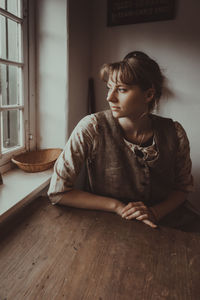 Woman looking away while sitting on table at home