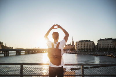 Male tourist making heart shape with hands in city against clear sky