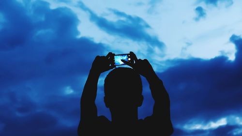 Low angle view of photographer photographing against sky