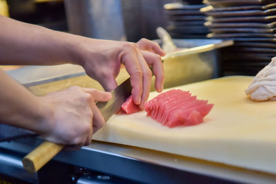 Cropped hand of chef cutting meat in commercial kitchen