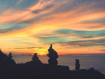 Silhouette stones stack on rocks against sky during sunset