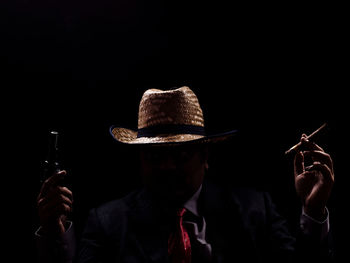 Man holding cigar and handgun against black background