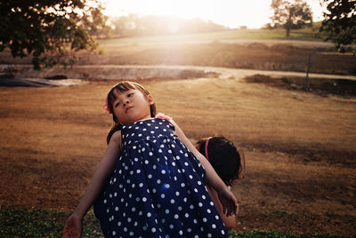 Sisters playing on field against sky during sunset